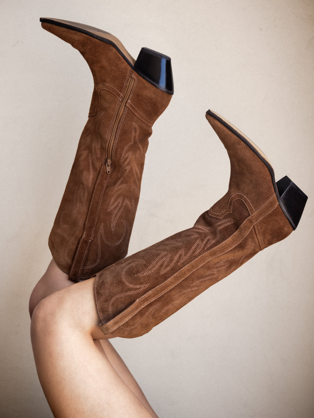 Brown suede knee-high boots with black soles on a neutral background