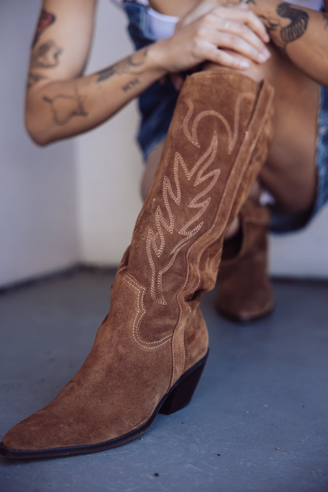 Close-up of brown western boots with light decorative stitching, styled with denim.