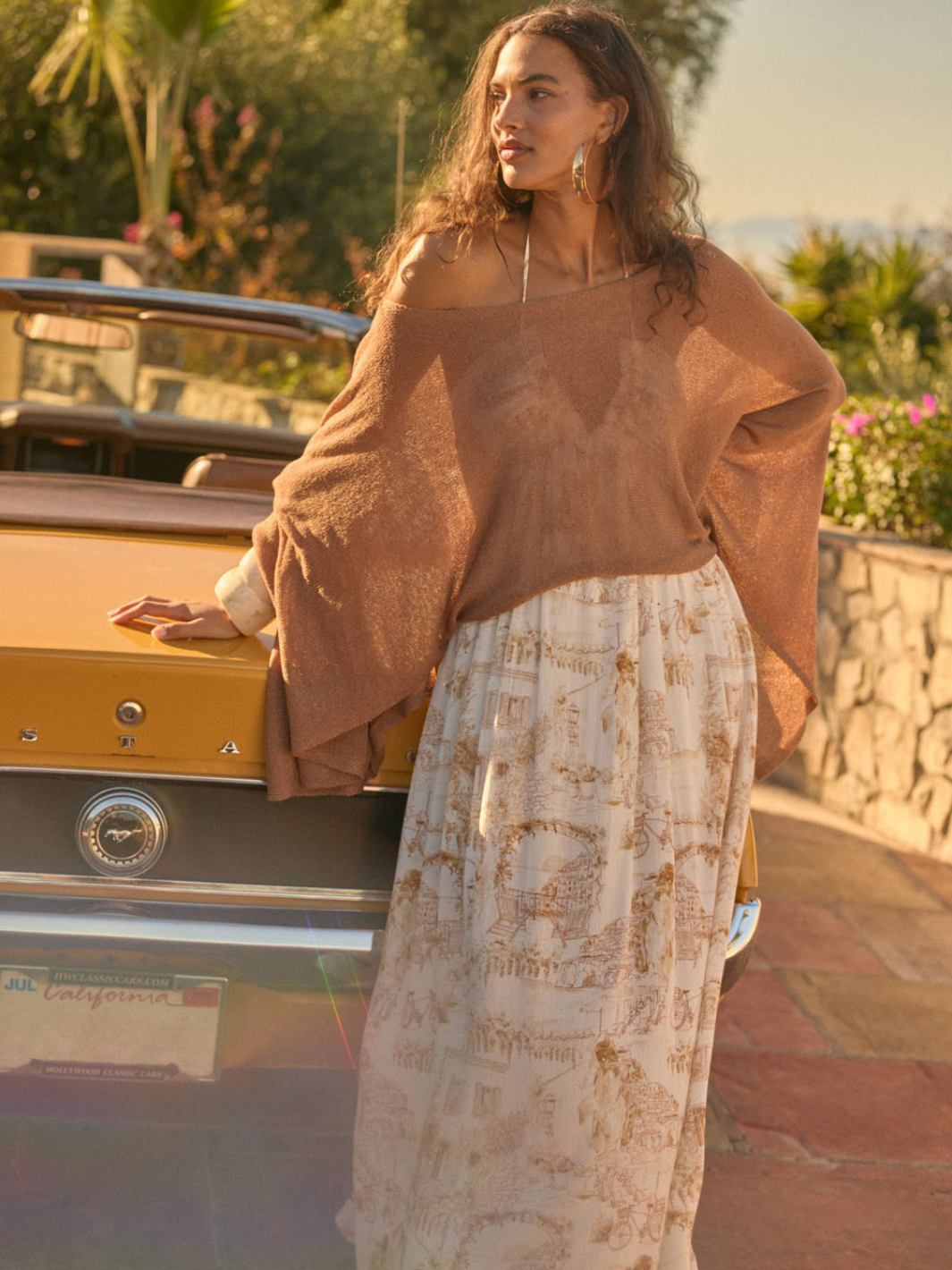 Daydrift Sheer Knit Poncho Sweater: oversized, airy caramel knit draped on woman beside a vintage car at golden hour.