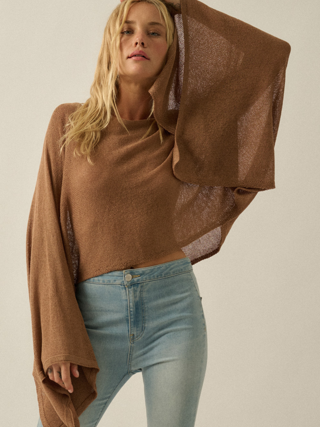Model wearing Daydrift Sheer Knit Poncho Sweater in warm brown; oversized, sheer knit with wide drape.