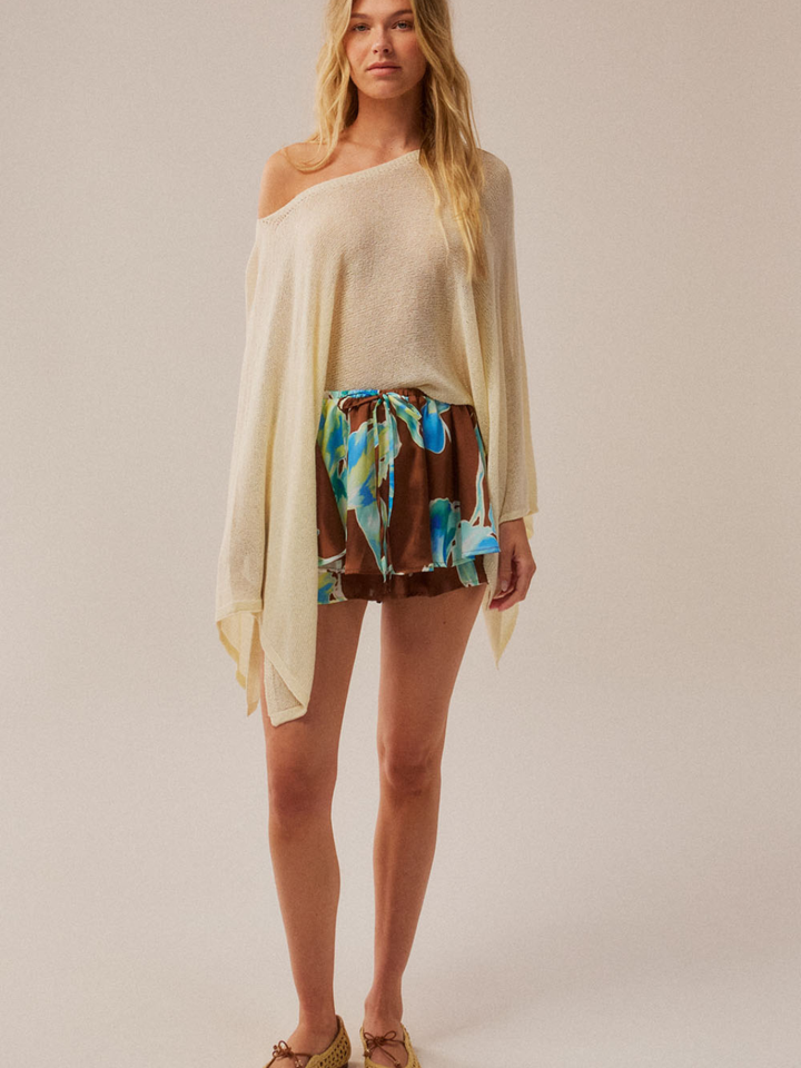 Daydrift Sheer Knit Poncho Sweater in ivory, oversized, draped poncho worn over a tropical-print skirt.