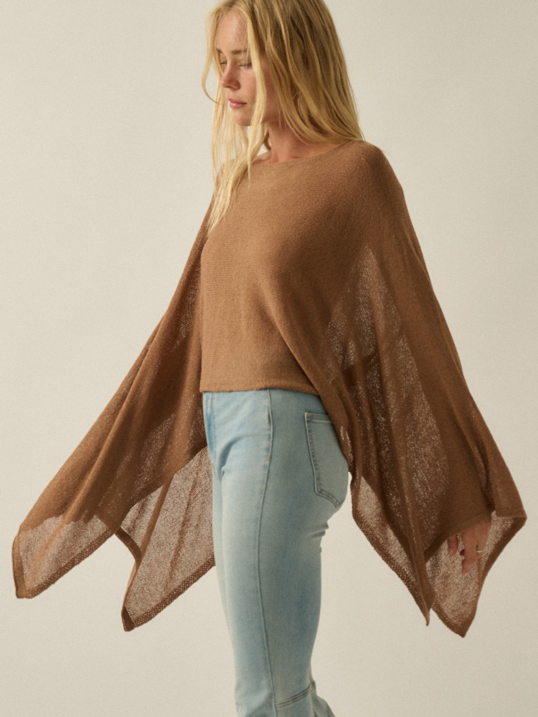 Daydrift Sheer Knit Poncho Sweater in camel, oversized and airy with a cloudlike drape over light-blue jeans.