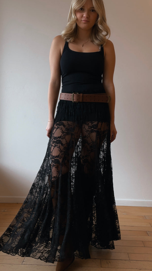 Woman wearing a black lace skirt and black top against a plain wall.