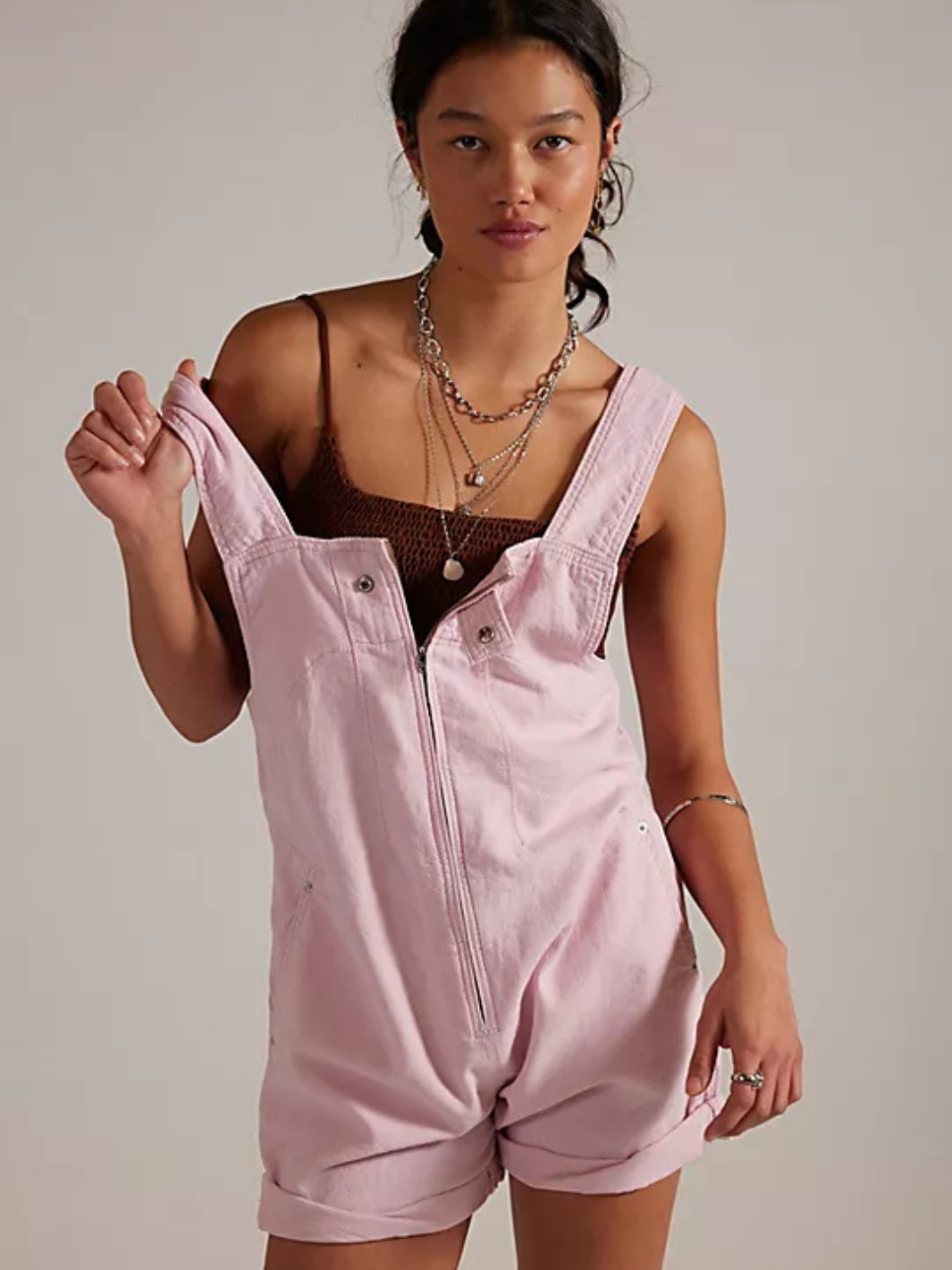 We The Free Jude Shortalls in pale pink on a model, zip-front, rolled cuffs, layered necklaces.