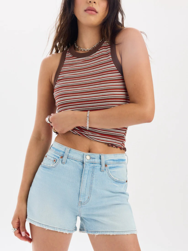 Model wearing DAZE DENIM Troublemaker high-rise cutoff denim shorts in light wash with stretch and a striped crop top.