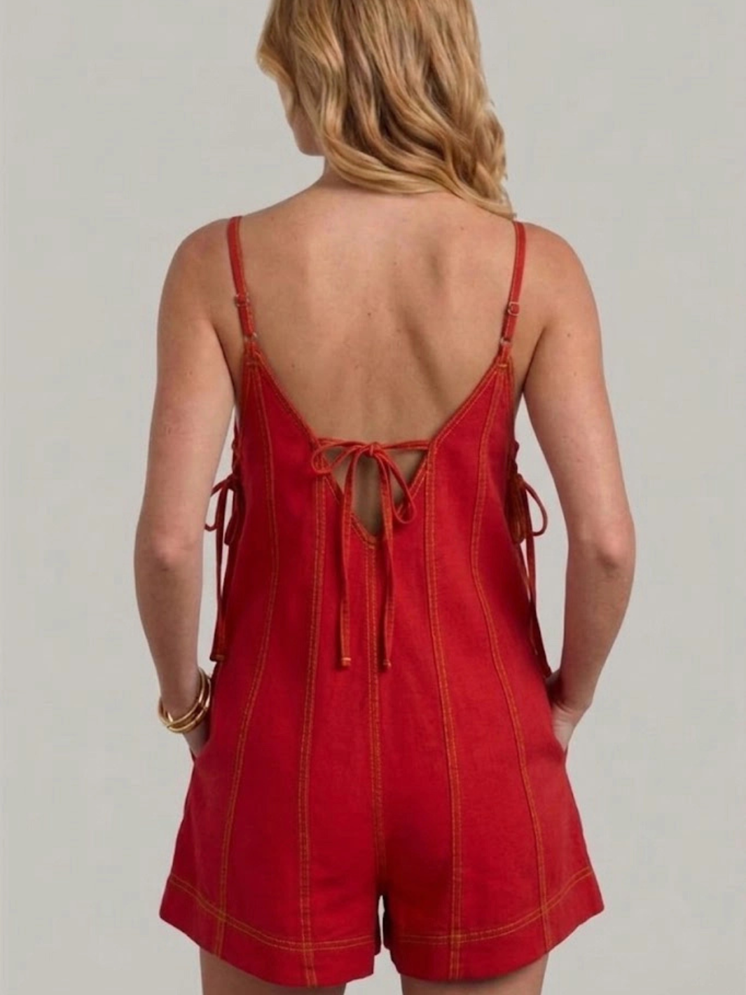 Cheyenne Contrast Stitch Cotton Romper in brick red – back view showing open back, center tie detail, adjustable spaghetti straps, mustard contrast topstitching, side ties, and side-seam pockets