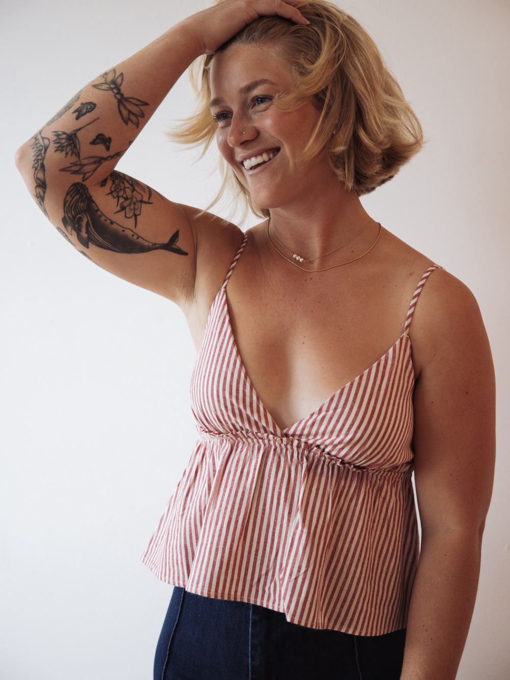 Smiling woman wearing The Sundrop red-and-white striped cotton babydoll tank top with peplum silhouette and smocking.