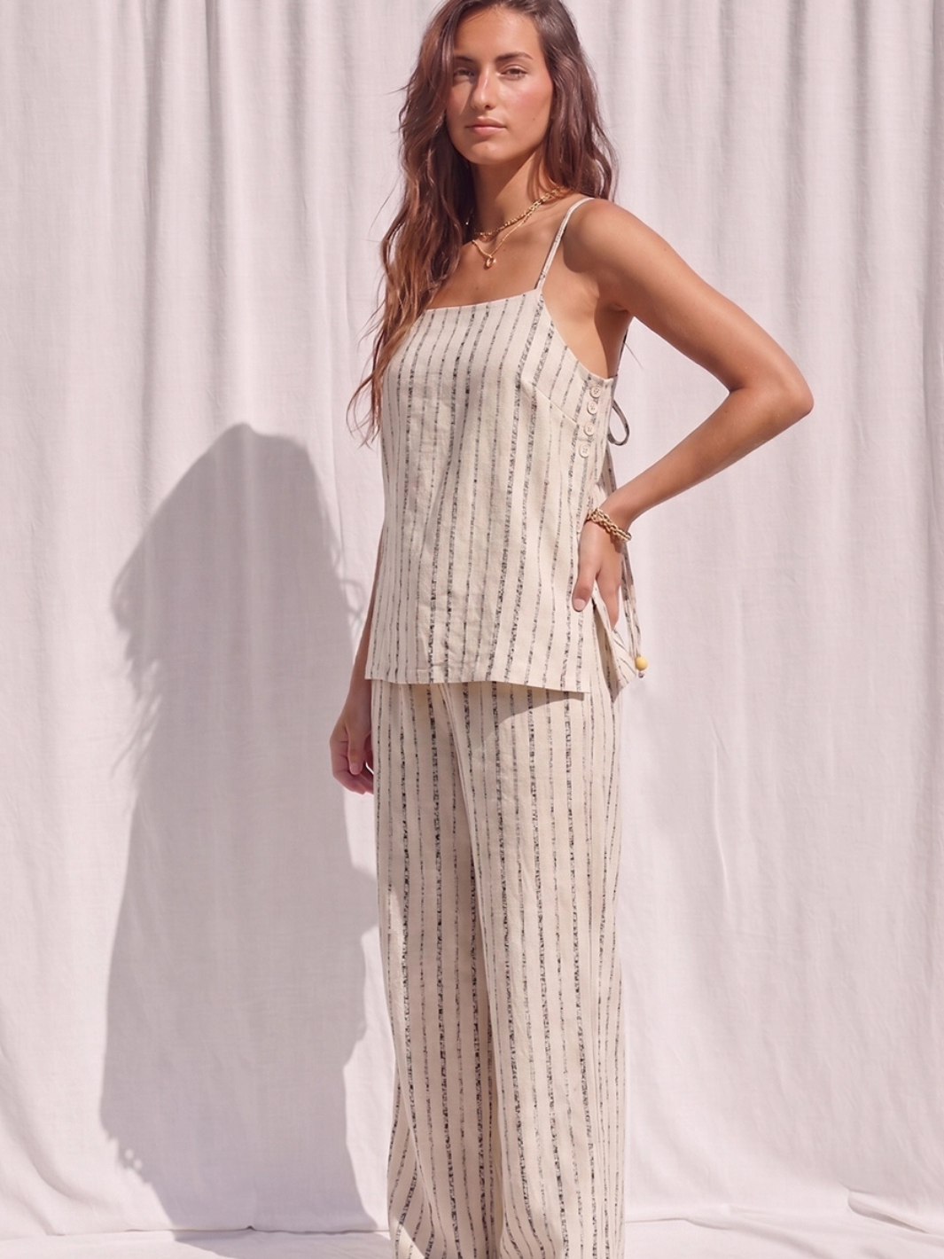 Model showcases The Coastal Stripe Square Neck Cami Top in beige stripes with open tie-back and beaded tassel.