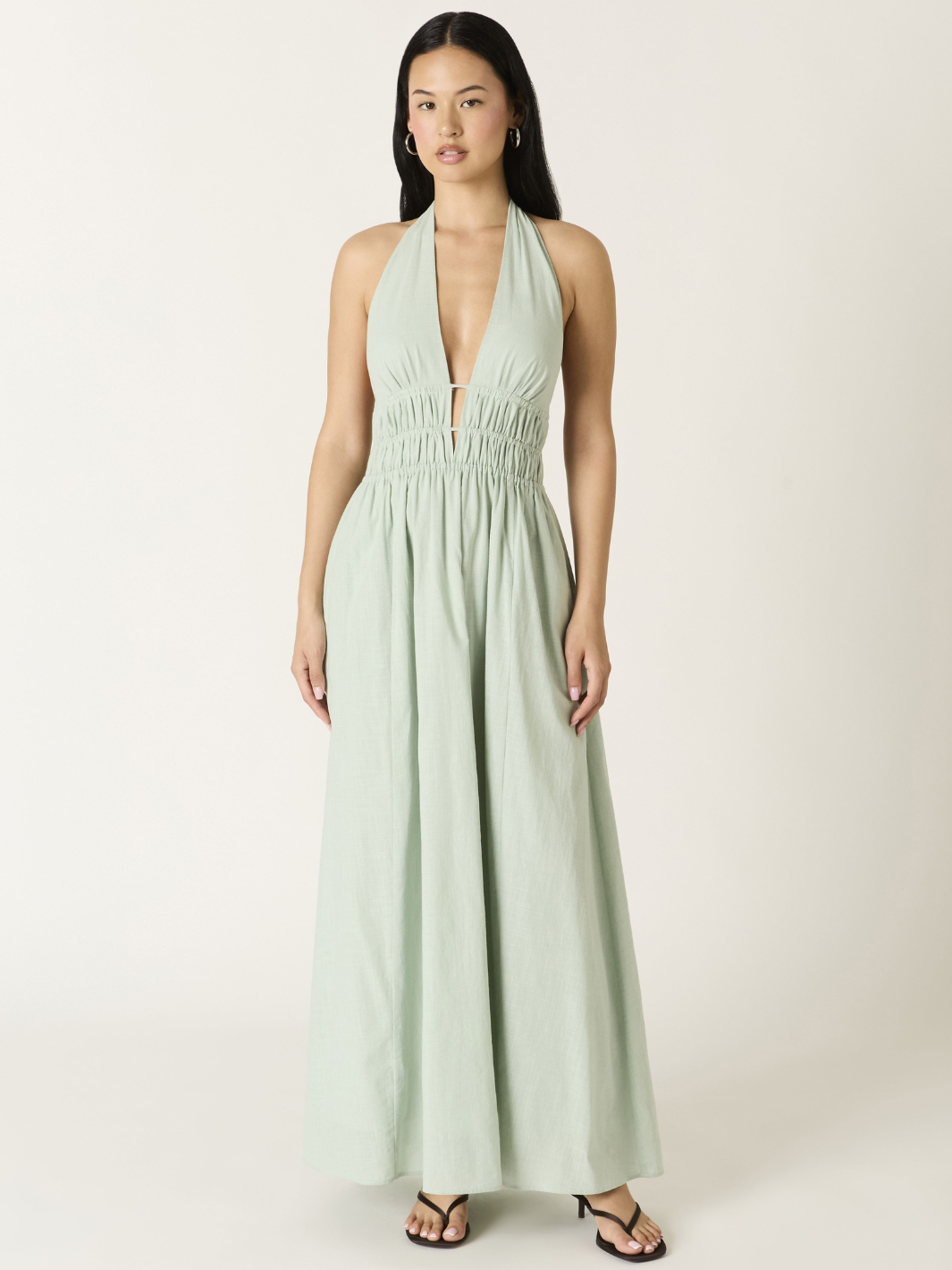 Soleil Plunge Halter Maxi Dress in sage green on a model with plunging neckline and ruched waist, flowing A-line skirt.