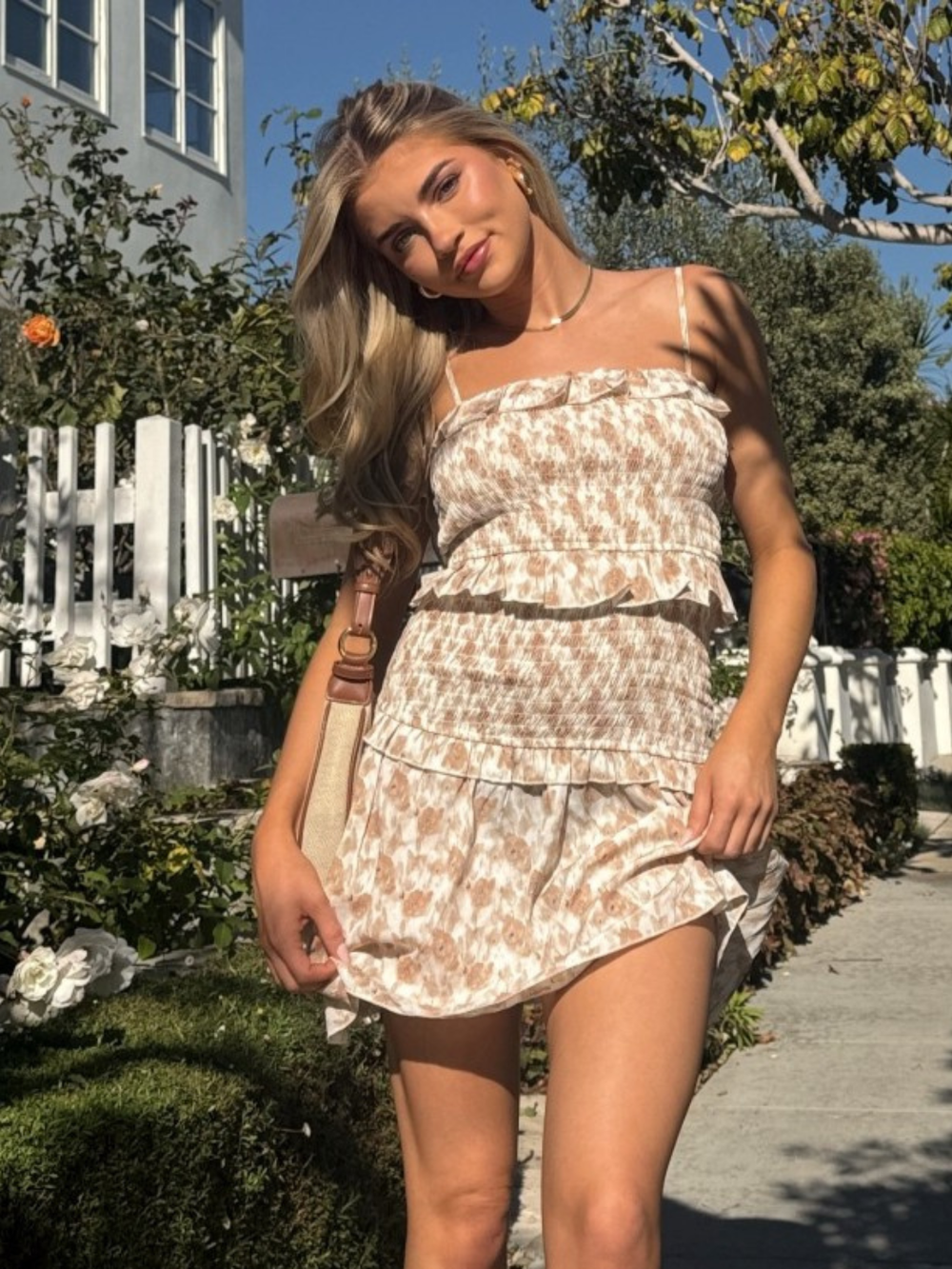 Model in Wildflower Smocked Ruffle Mini Dress, beige floral print with smocked bodice and tiered ruffles, outdoor sun.