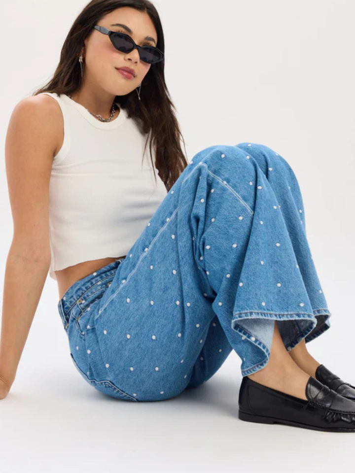Model in Daze Denim The Wanderer mid-rise palazzo jeans with blue polka dots, white top, and black loafers.