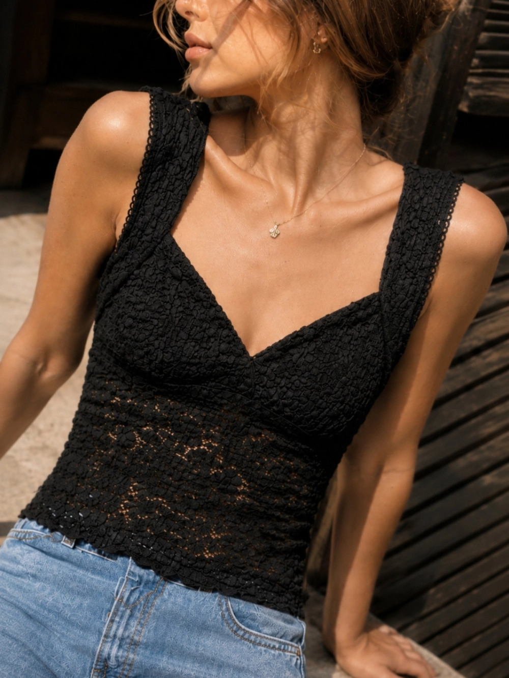 Model wearing The Noir Floral Lace Cropped Tank Top in black semi-sheer lace with blue jeans.