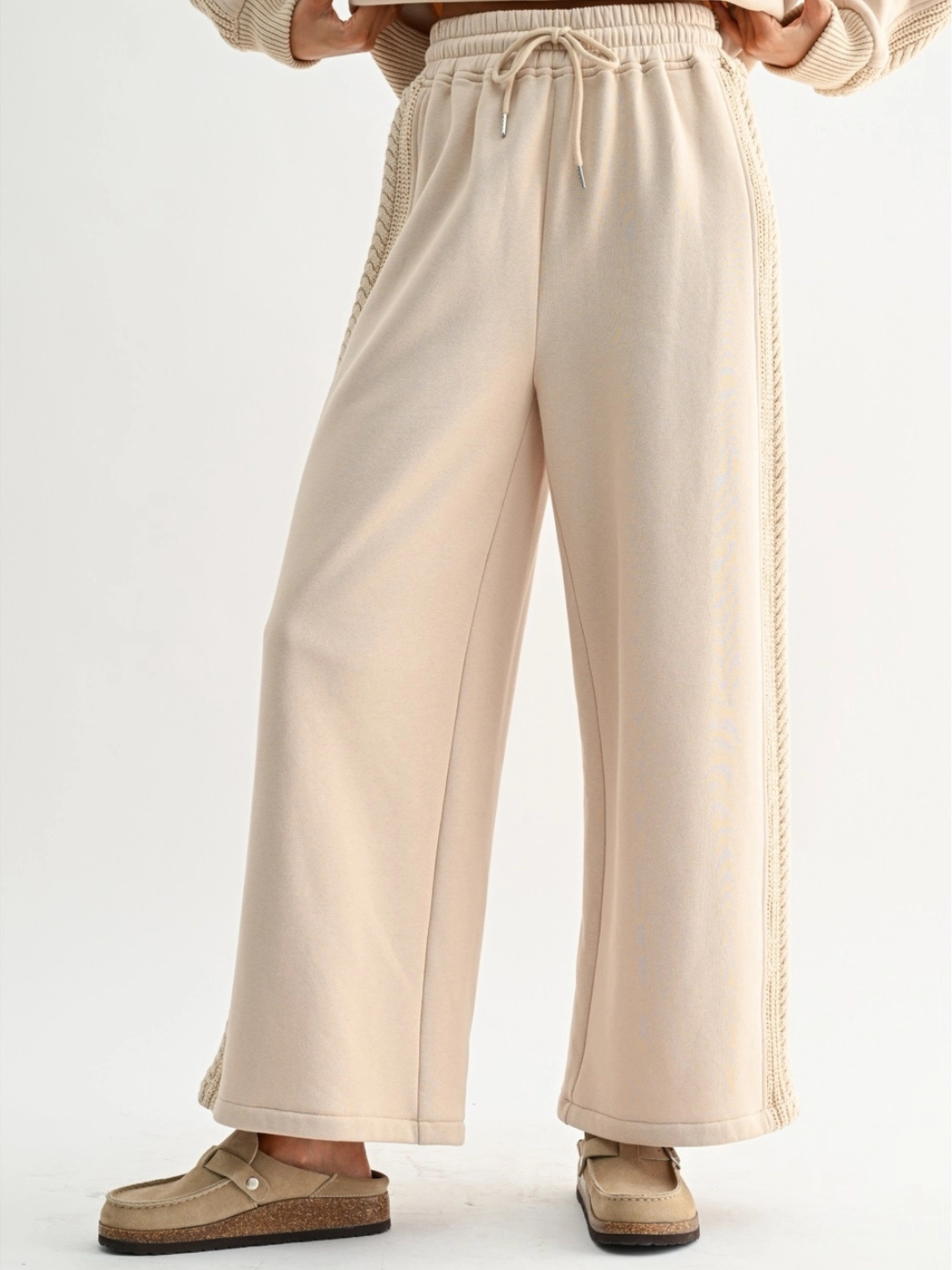 Beige wide-leg knit pants with braided side trim and drawstring waist, paired with tan loafers.