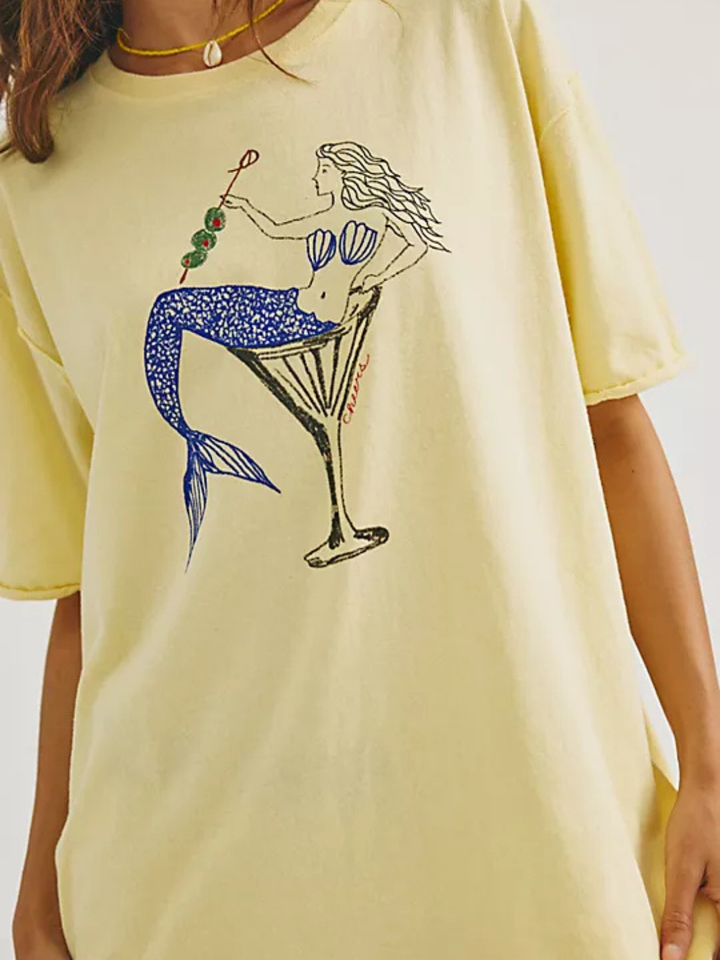Oversized pale yellow tee with mermaid in a martini glass and olive skewer graphic.