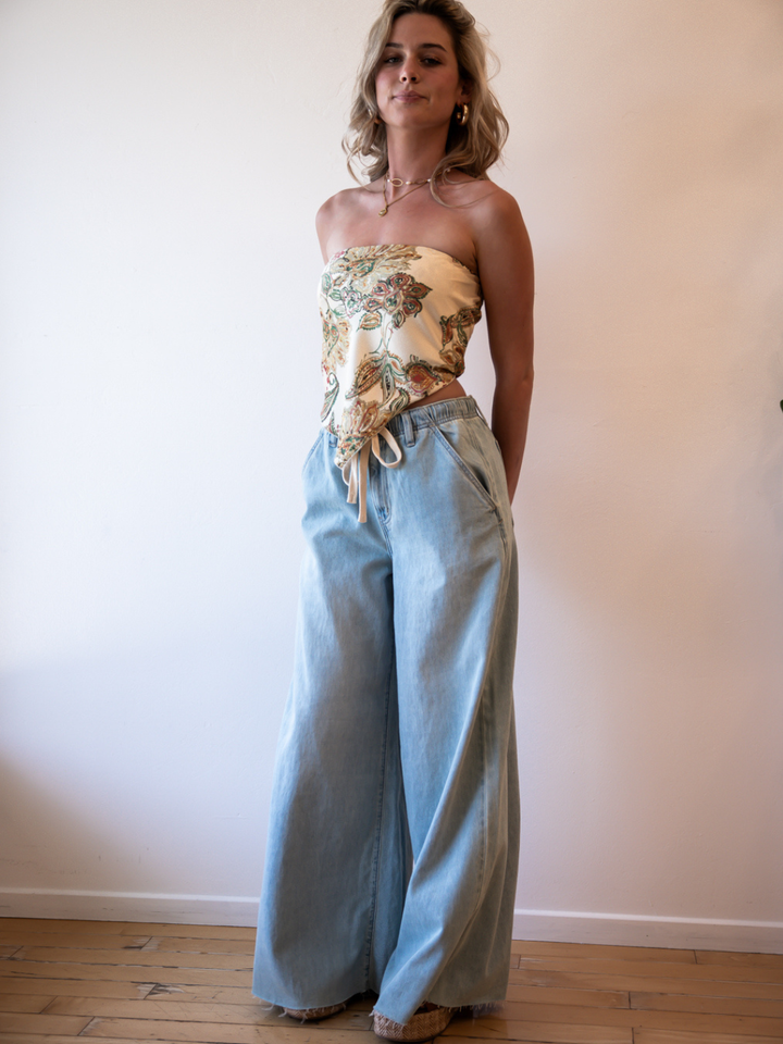 Model in Daze Denim Cabana Wide Leg Pull-On Jeans, light wash, floral strapless top—vacation-ready.