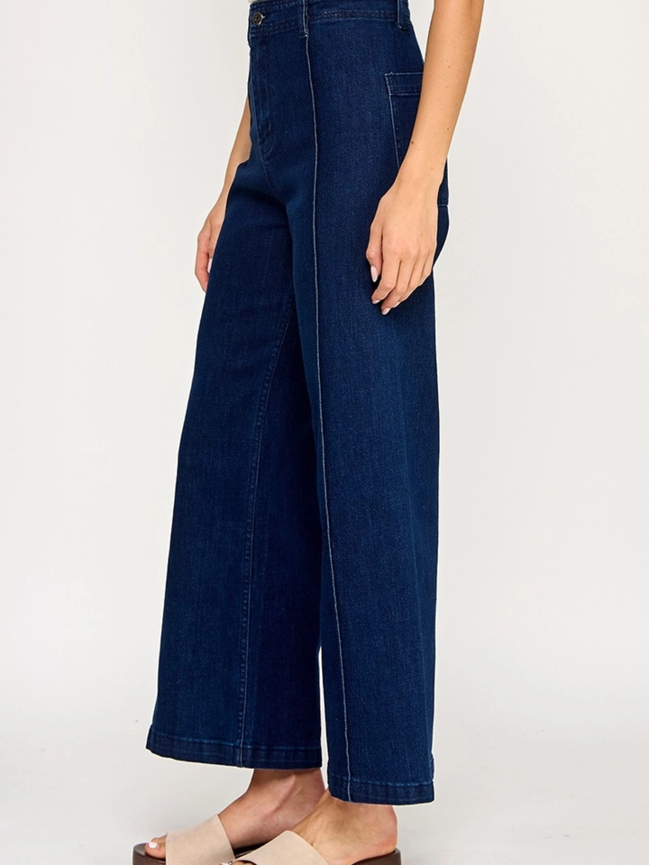 Full-length front view of The Sundaze dark indigo high-rise wide-leg stretch jeans with elongating front seam detail, styled with a cream lace crop top, boho headscarf, and neutral block heel sandals