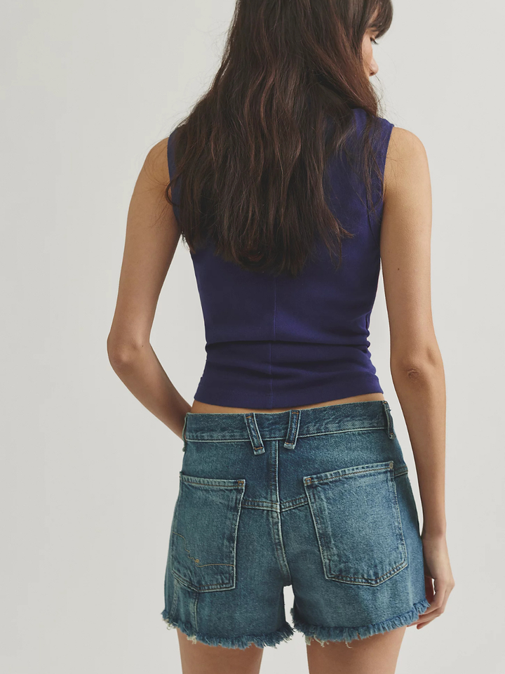 Back view of a model wearing Free People Now Or Never Denim Shorts with a frayed hem and purple top.