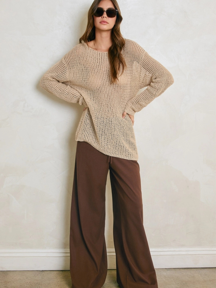 Model wearing Sandcastle Open-Knit Pullover Sweater in natural taupe with wide-leg brown pants.
