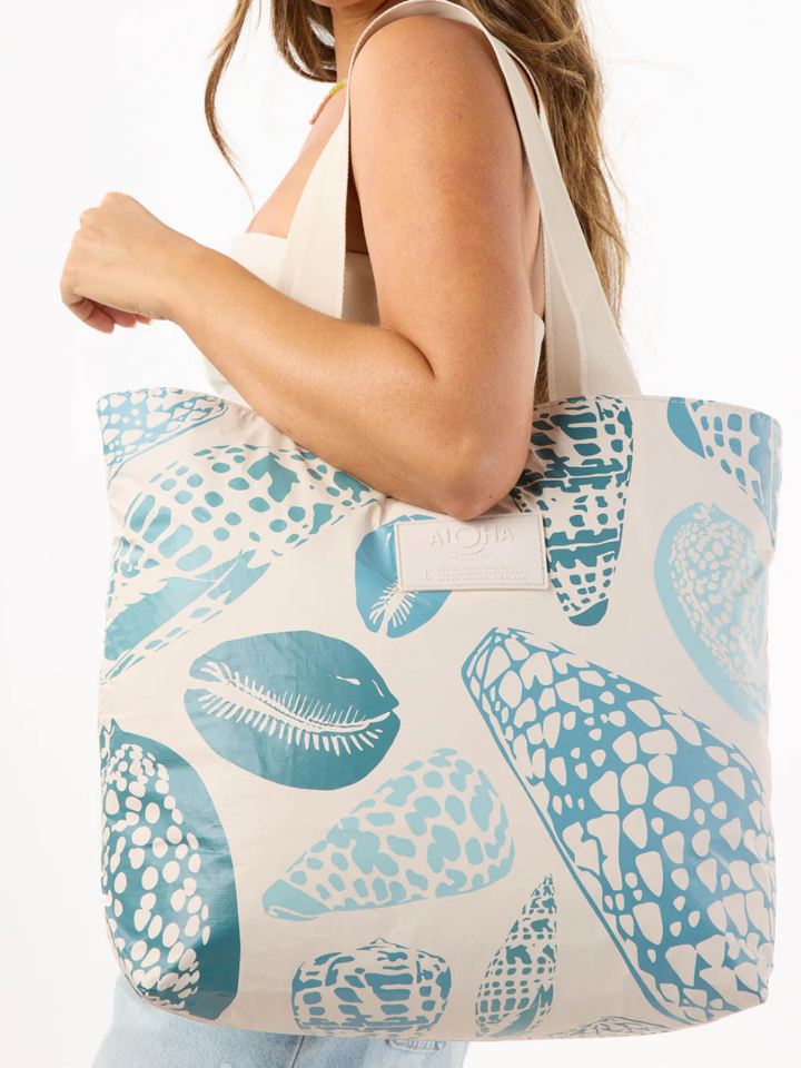Shoreline tote from the ALOHA Collection featuring blue seashell print and white straps carried by a model.