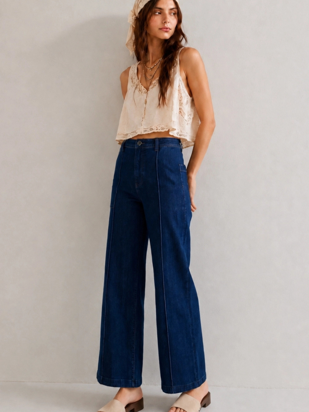The Sundaze Dark Indigo High-Rise Wide-Leg Stretch Jean with front seams, paired with cream lace top; retro 70s vibe.
