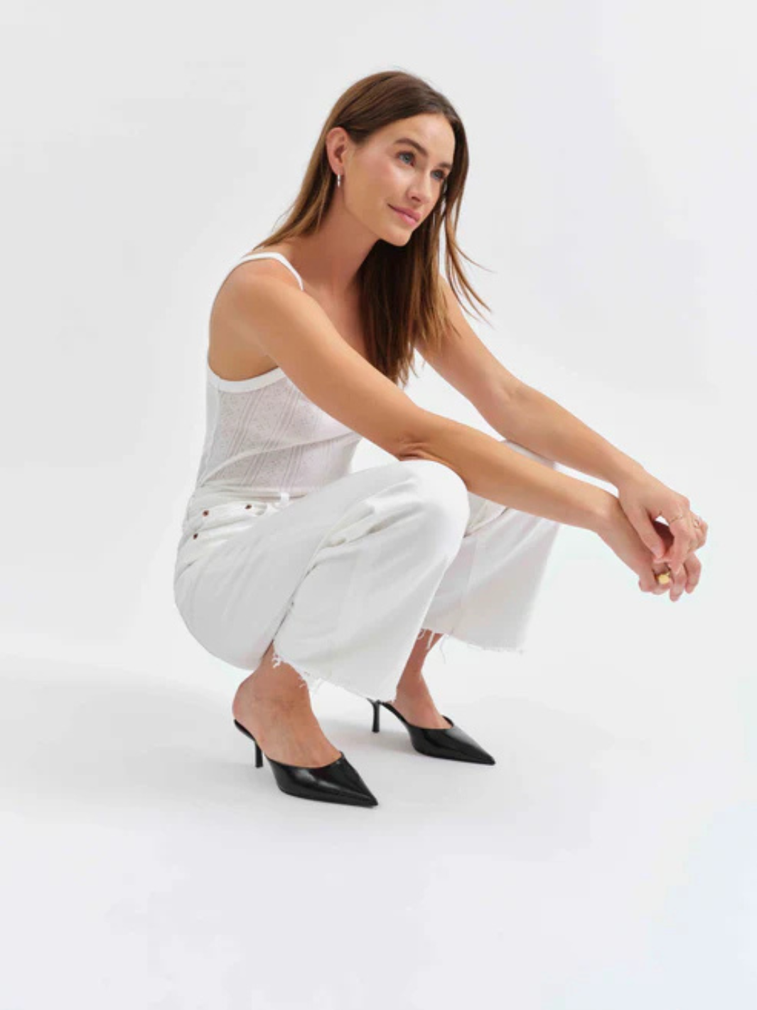 Model crouched in white outfit with black heels; DAZE DENIM Pleaser high-rise wide-ankle jeans in indigo wash.