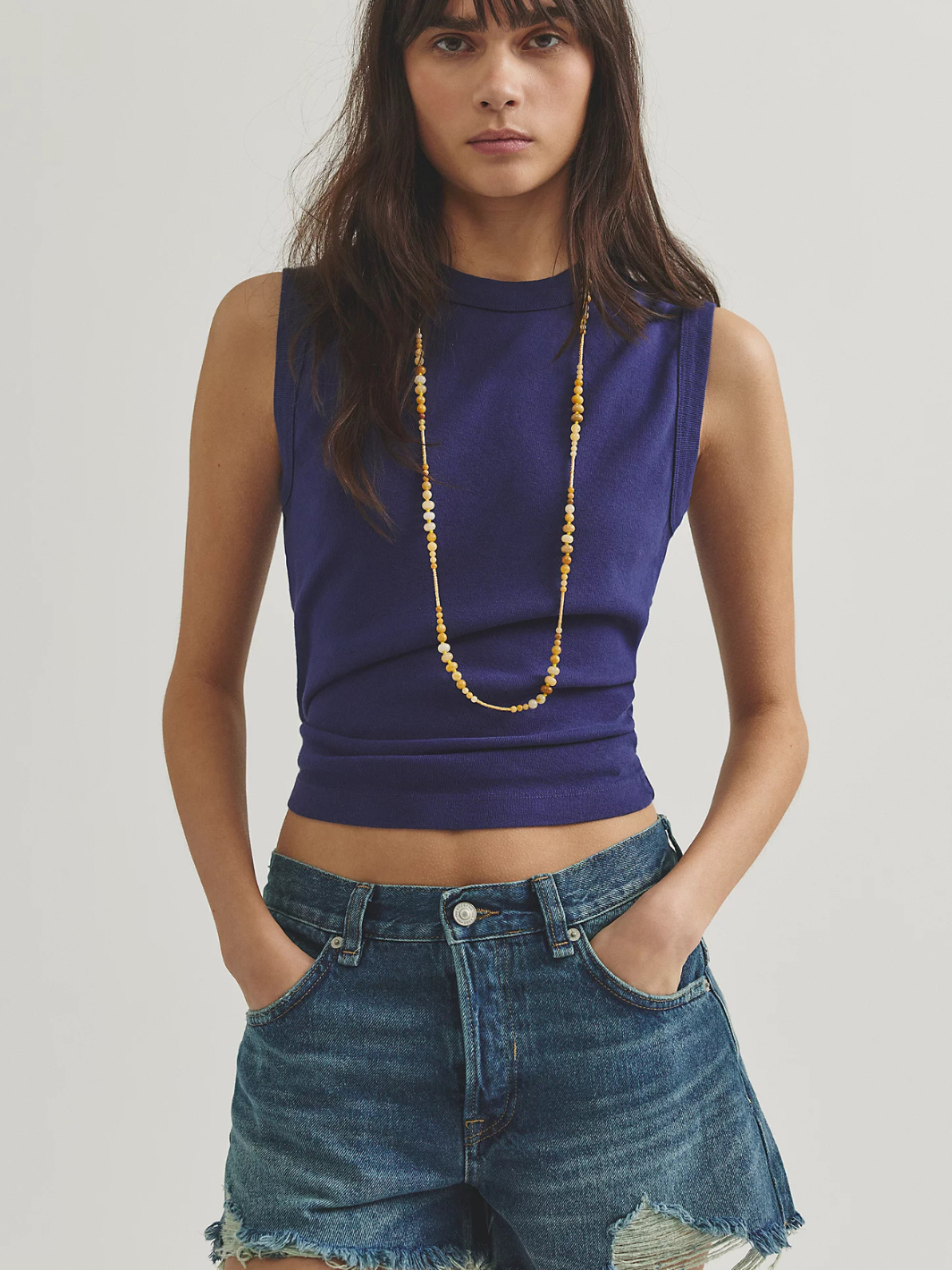 Free People Now Or Never Denim Shorts on a model in a purple sleeveless top, featuring frayed hems.