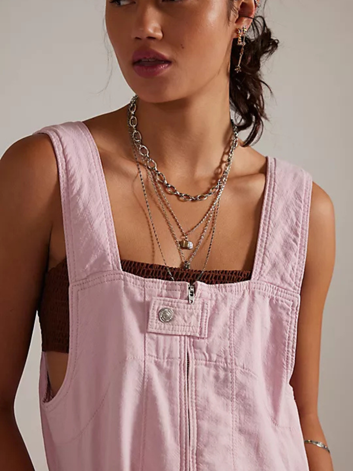 We The Free Jude Shortalls in pink with front zip and metal snap, styled with layered necklaces.