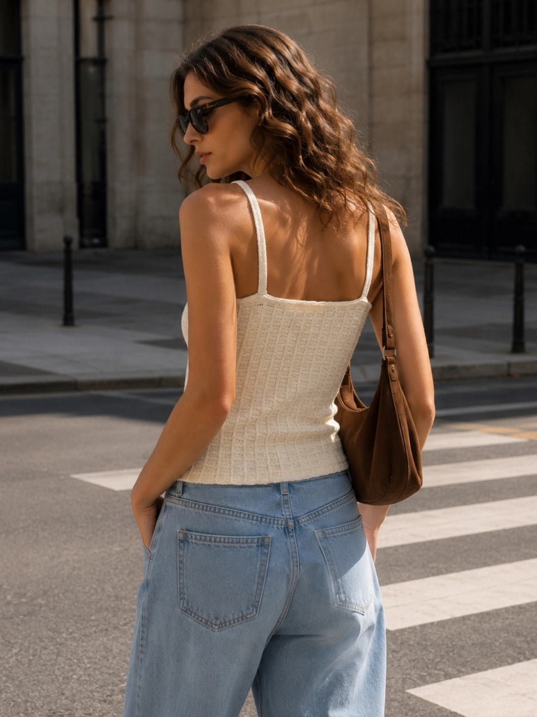 Back view of cream waffle-knit spaghetti strap cropped camisole with ribbed texture and raw hem edge, styled with wide-leg light wash jeans on city street