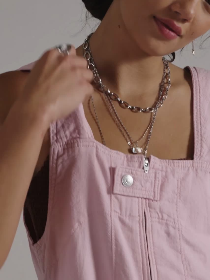We The Free Jude Shortalls in soft pink with front pocket, shown with layered silver necklaces.
