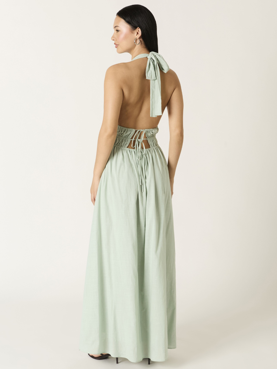 Back view of a sage-green Soleil Plunge Halter Maxi Dress with open back, tie at waist, and flowing A-line skirt.
