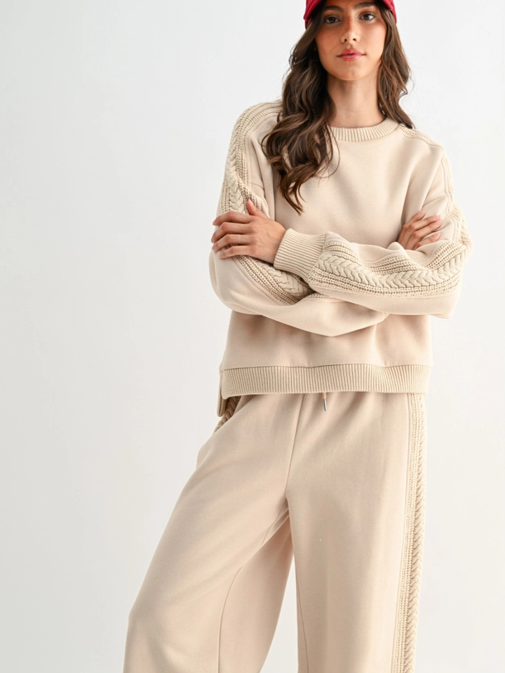 Model wearing The Aria Cable Knit Sweatshirt in beige with cable-knit sleeves and matching lounge pants.