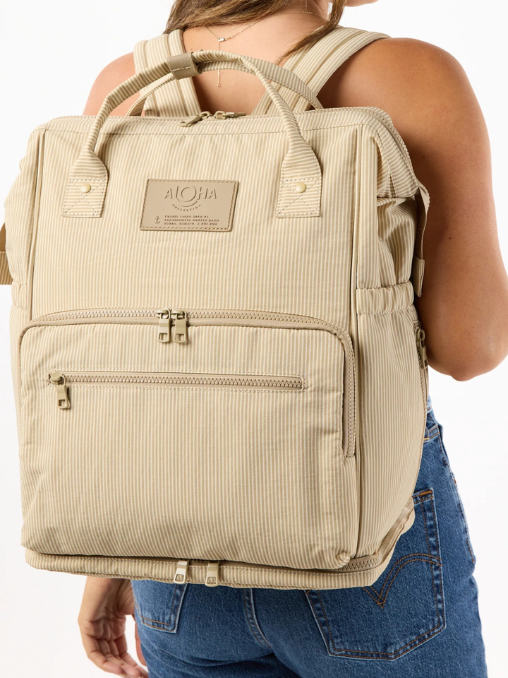 ALOHA Collection Le Bébé Diaper Backpack in beige striped fabric worn on a person’s back.
