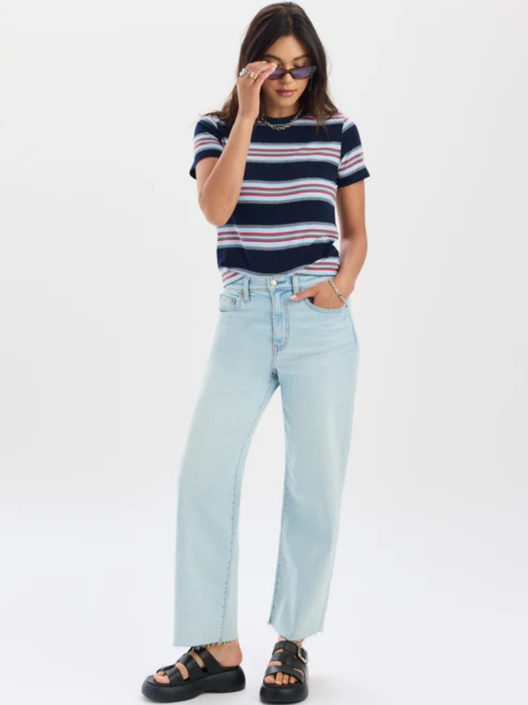 Model wearing DAZE DENIM Pleaser High Rise Wide Ankle Jeans in light indigo wash with striped top and sandals.