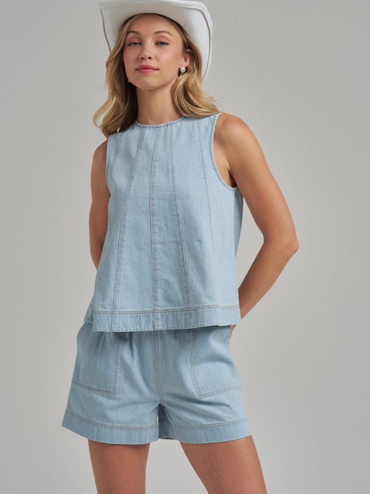 Model in light-blue Sutton Pinstripe Denim Shorts with panel-seam structure and matching sleeveless top and hat.