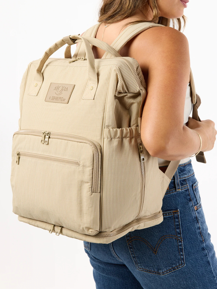 ALOHA Collection Le Bébé Diaper Backpack in beige stripes, worn by a person in denim jeans.