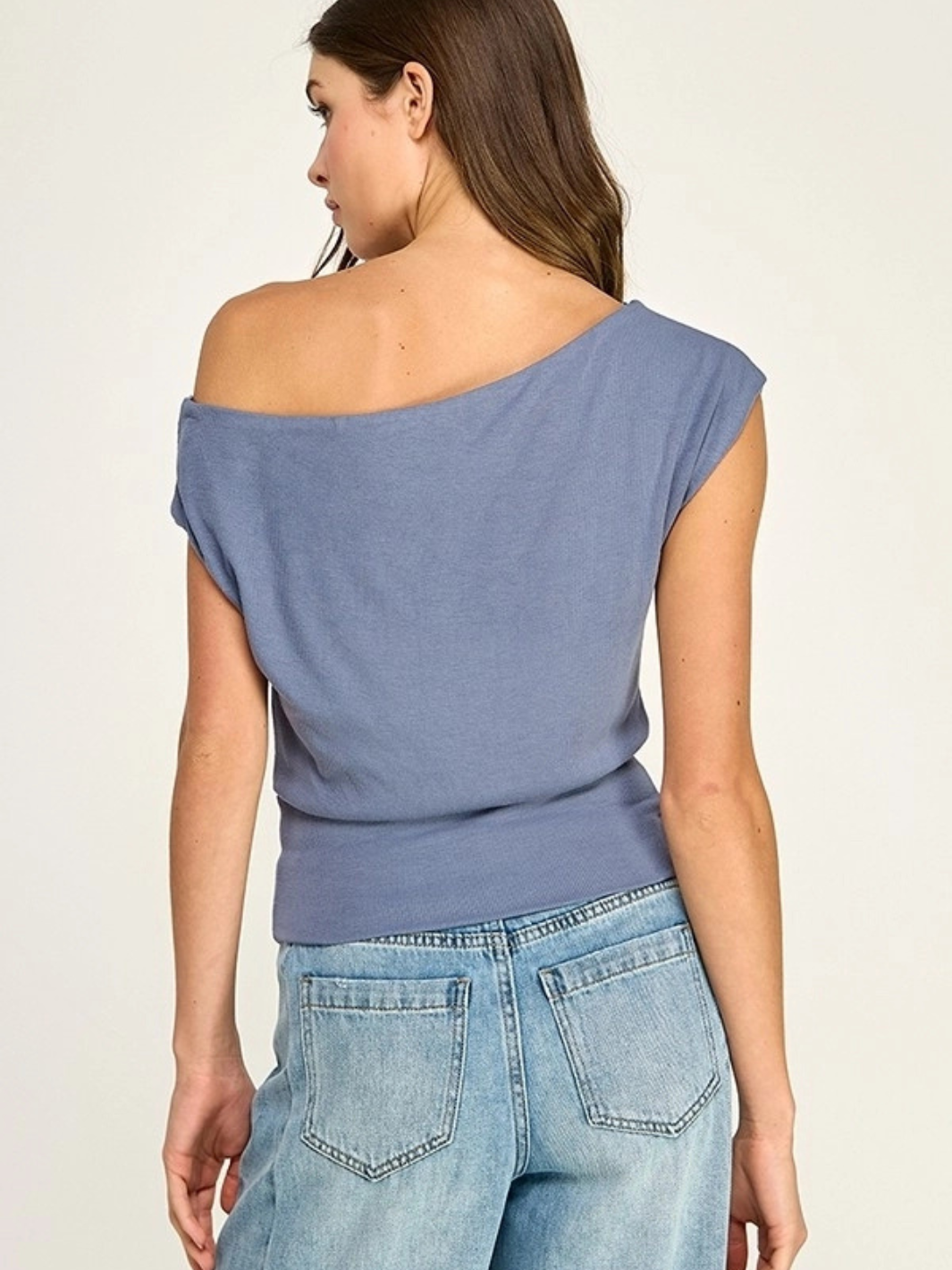 Back view of Malibu Slate Blue Off-Shoulder Stretch Knit Top on a model, paired with light denim jeans.