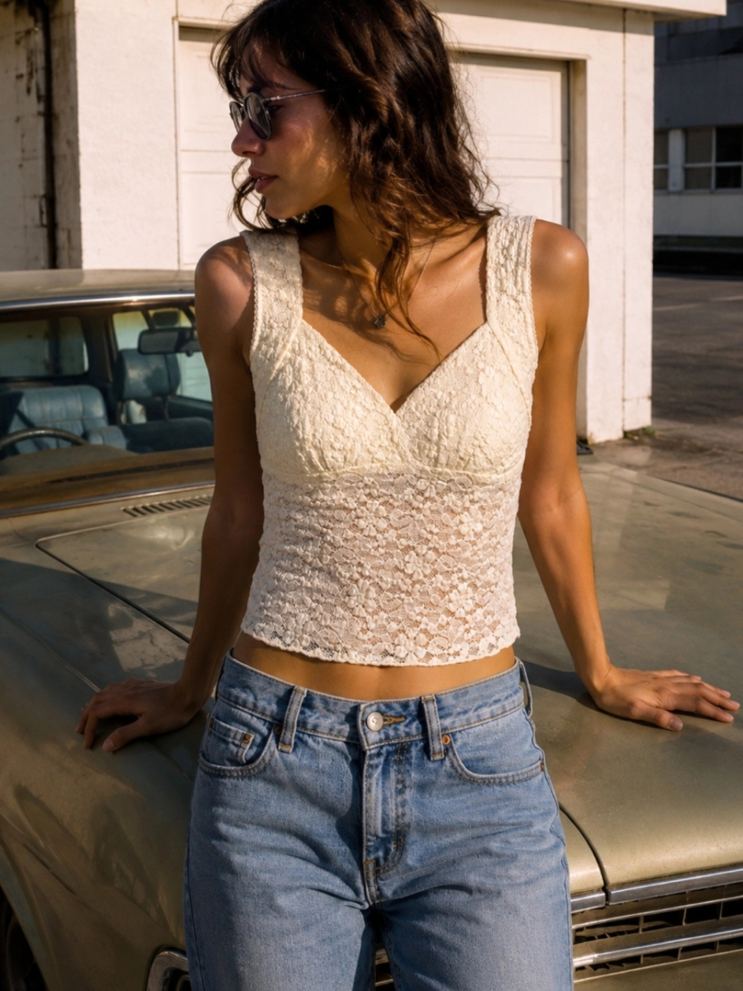 The Noir Floral Lace Cropped Tank Top worn by a woman in ivory lace, paired with blue jeans outdoors.