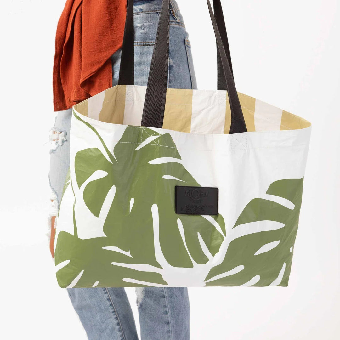 Aloha Collective Monstera Seaweed tote with bold green monstera leaf print on white canvas and black handles.