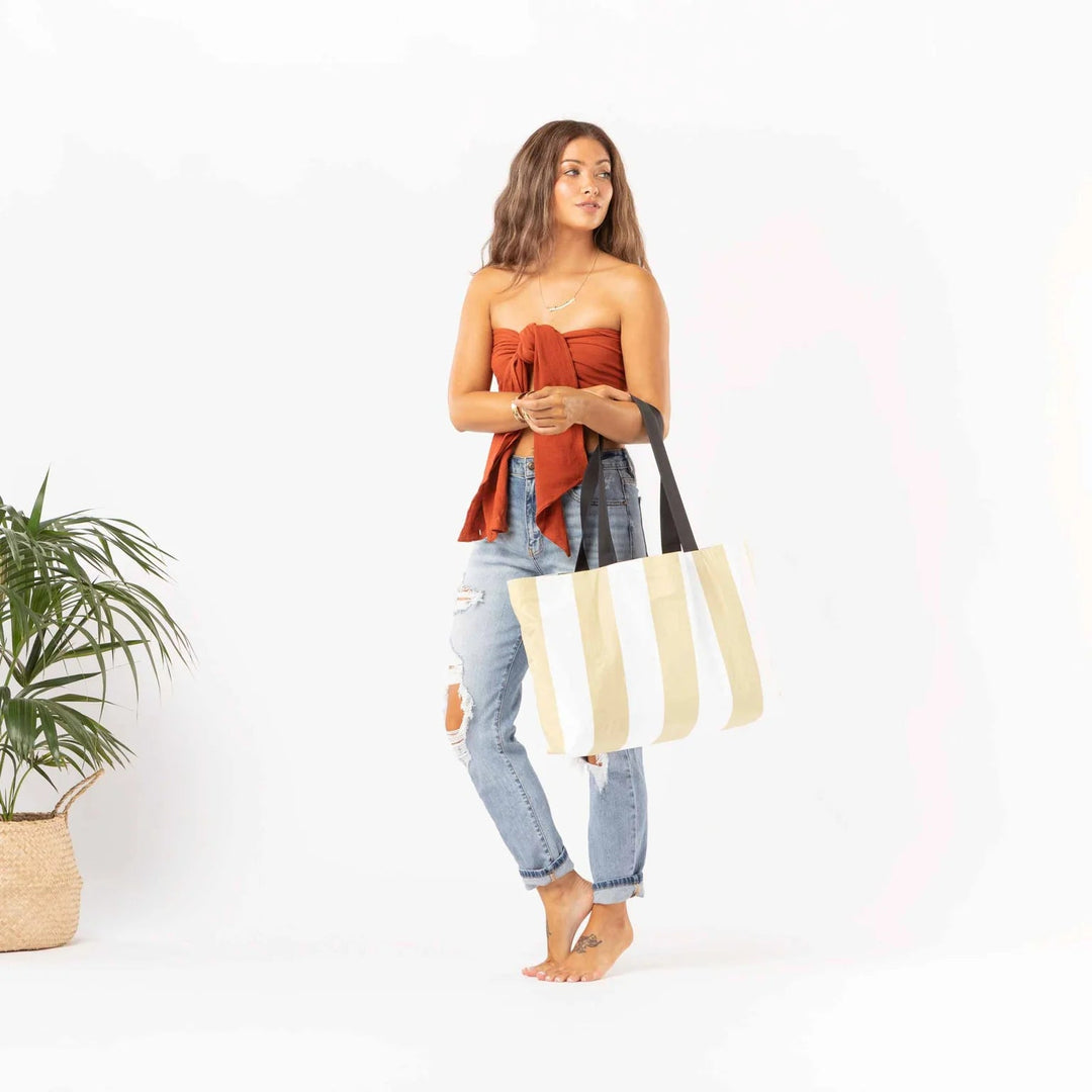 Woman in orange strapless top and distressed jeans holds a striped tote, tropical Monstera Seaweed print vibe.