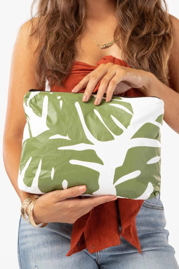 Aloha Monstera Seaweed clutch with bold green monstera leaves, held by a woman.