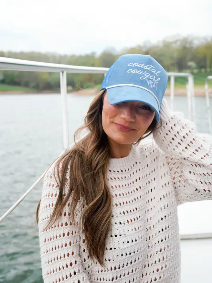 Coastal Cowgirl blue corduroy trucker hat with white rope, worn by a smiling woman on a boat.