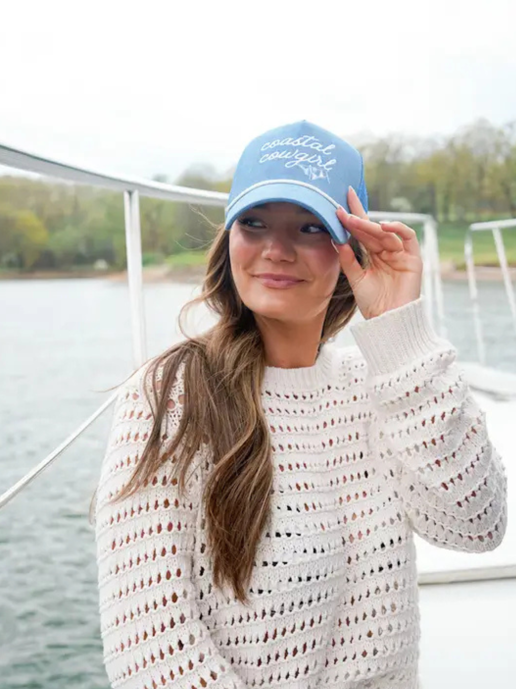 Coastal Cowgirl blue corduroy trucker hat with white rope embroidery worn by a woman on a boat