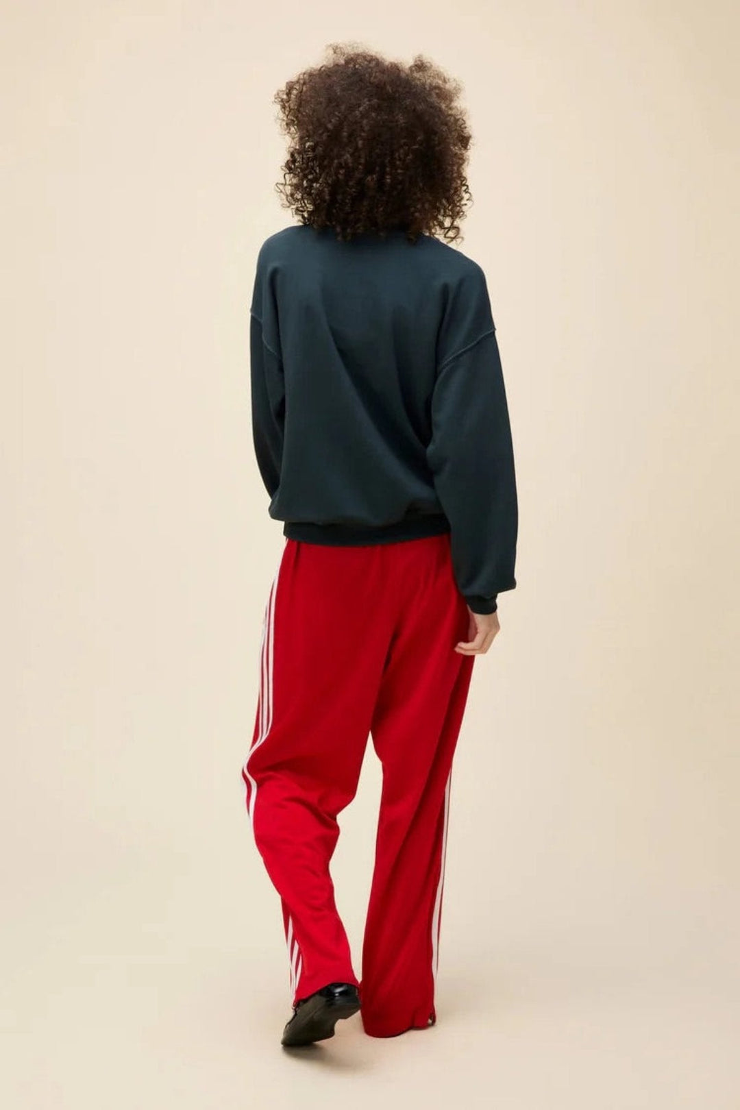 Person in a graphic sweatshirt and red track pants standing with hands on hips.