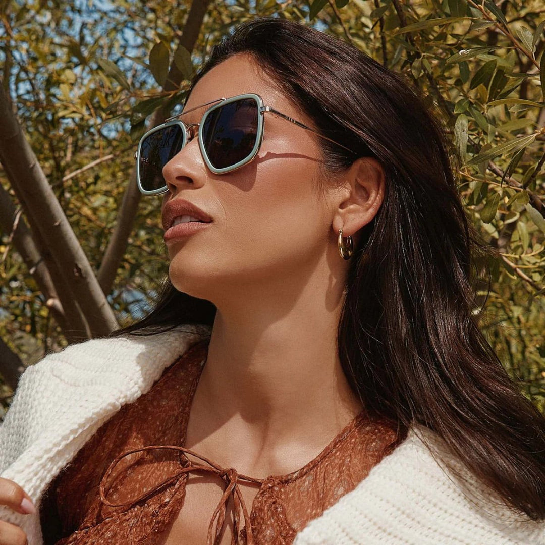 Square-framed sunglasses with gold metal arms and dark lenses on a white background.