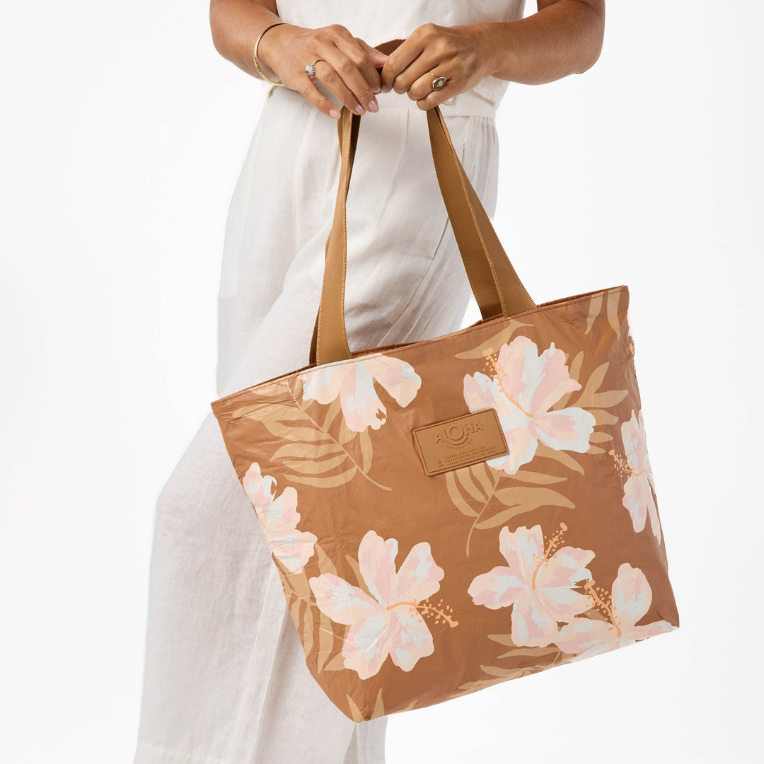 Toffee-brown Adrift Day Tripper tote with cream and blush hibiscus blooms and palm fronds, carried by its toffee straps