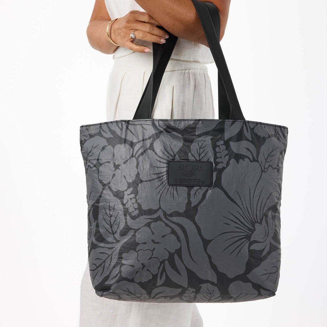 Woman in white linen carrying the Heipua Day Tripper tote on her arm, showing the tonal hibiscus print