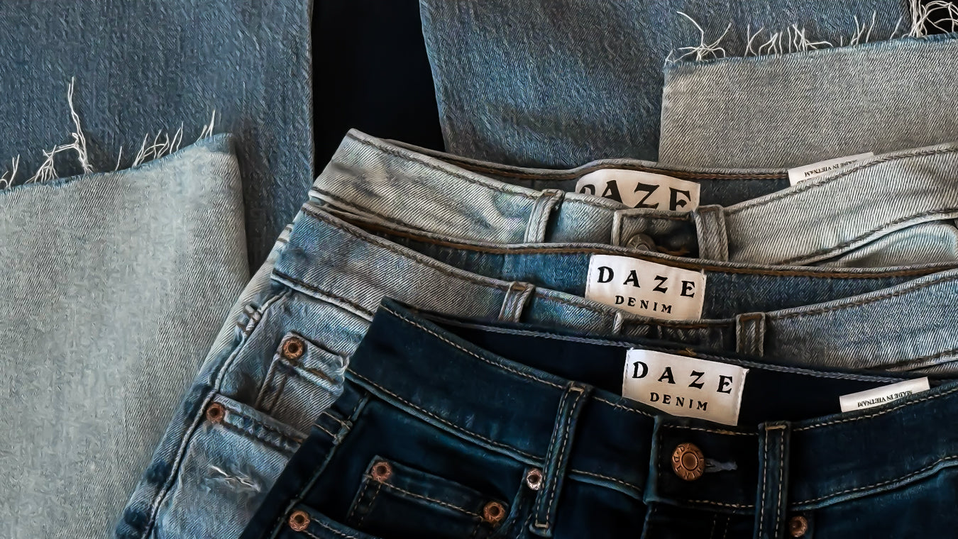 Stack of jeans with 'DAZE Denim' labels on a textured surface