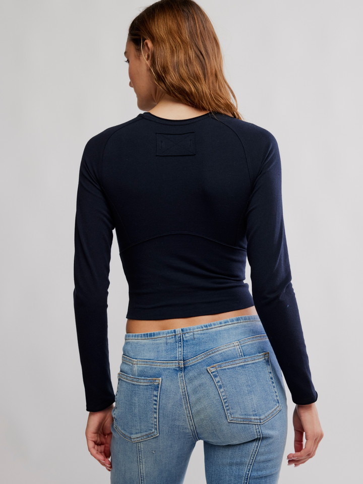 Navy Protagonist Long Sleeve top on model, back view with cropped hem, curved seam, paired with jeans.