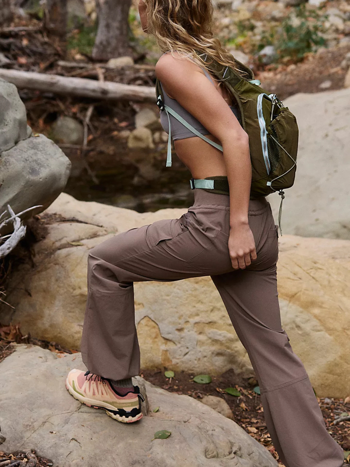 Woman climbing a rock in the FREE PEOPLE - Cool Climber Pant Solid, perfect for outdoor adventures and casual outings.