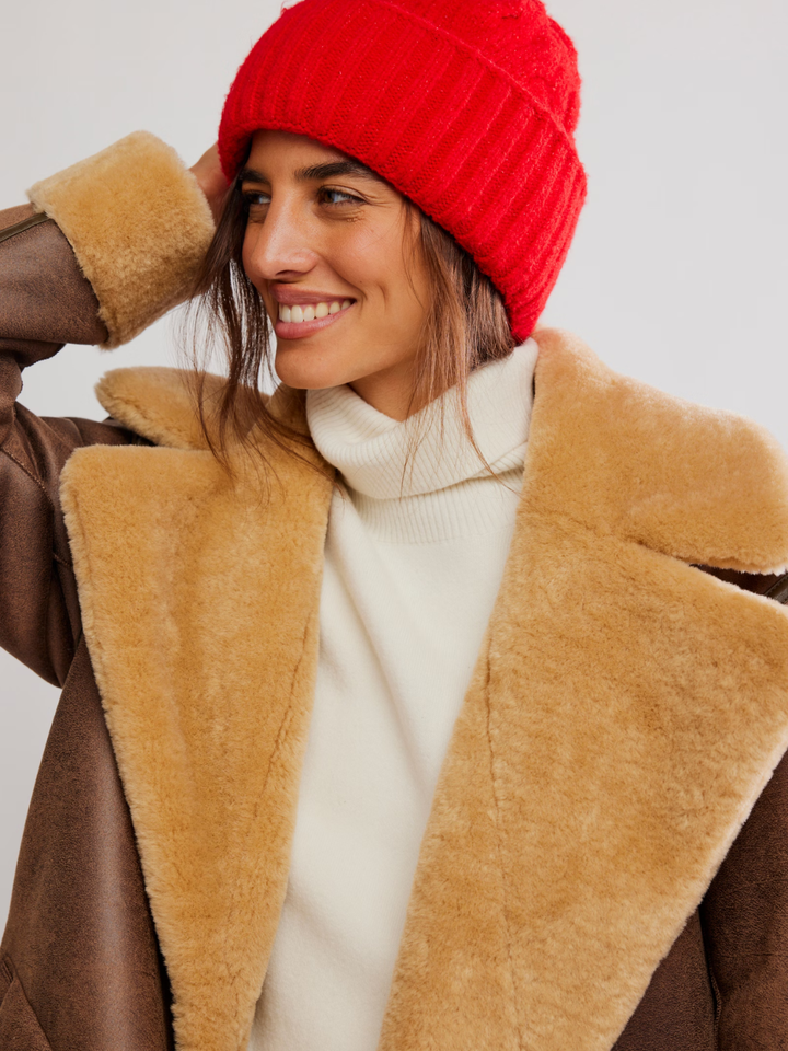 FREE PEOPLE Coast Line Beanie in red, paired with tan shearling coat and white turtleneck.
